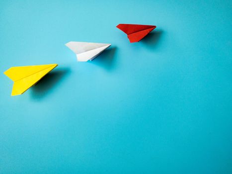 Red paper airplane origami leading white and yellow airplanes on blue background with customizable space for text. Leadership skills concept