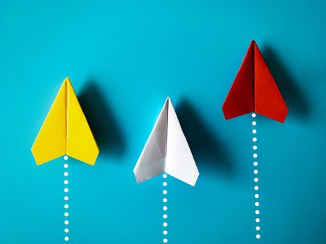Yellow, white and red paper airplane origami racing to achieve destination on blue background with customizable space for text. Business goals concept.