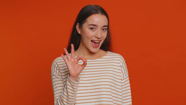 Ok. Joyful happy pretty woman in pullover looking approvingly at camera showing approve feedback gesture like sign positive something good. Young girl on red studio background. People sincere emotion