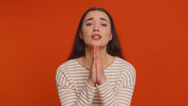 Please, God, forgive me. Young woman sincerely praying to God and looking up with pleading expression, begging apology, beseeching with hopeful face. Millennial girl isolated on red studio background