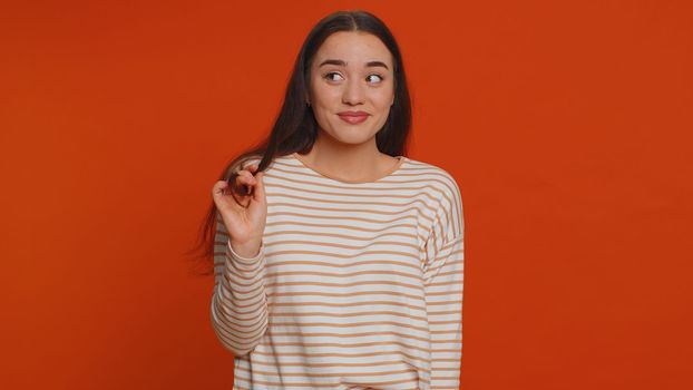 Smiling playful pretty young woman in pullover blinking eyes, looking at camera with toothy smile, winking and flirting, expressing optimism. Millennial happy girl isolated on red studio background