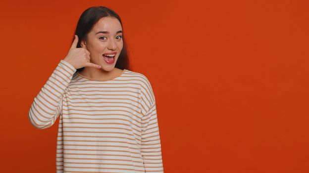 Call us, here is contact number. Young woman looking at camera doing phone gesture like says hey you call me back, conversation. Caucasian girl showing advertising area isolated on red background
