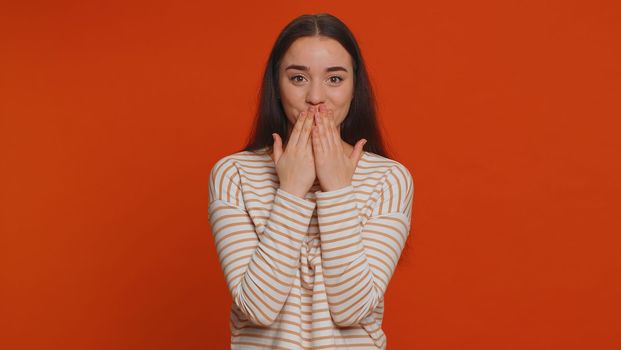I will not say anyone. Frightened woman closing her mouth with hand, looking intimidated scared at camera, gestures no, refusing to tell terrible secret, unbelievable truth. Girl on red background