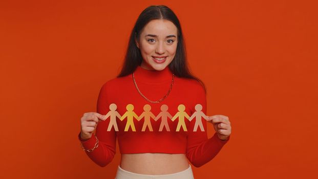 Woman showing multiracial different skin color human shape cut out of paper, concept of teamwork, partnership, community, unity, people support love, against racism. Young girl on red background