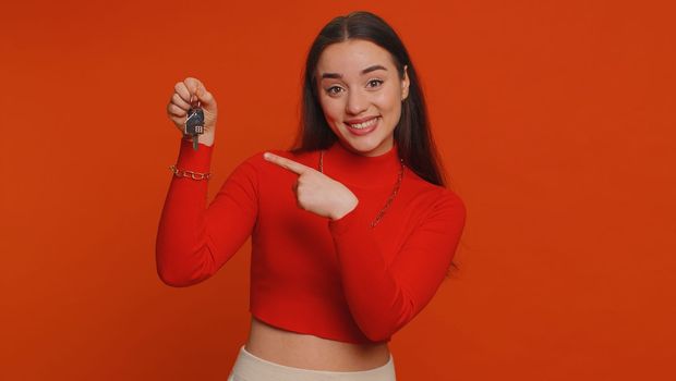 Pretty young woman in crop top real estate agent lifting hand showing the keys of new home house apartment, buying, renting property, mortgage loan. Millennial girl isolated on red studio background