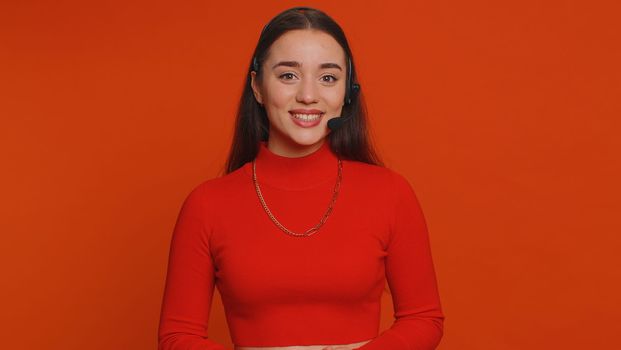 Smiling pretty woman wearing headset, freelance worker, call center or support service operator helpline, having talk with client or colleague, communication support. Young girl on red background