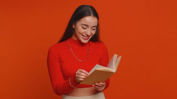 Happy pretty woman reading funny interesting fairytale story book, leisure hobby, knowledge wisdom, education, learning study, wow inspiration. Young adult girl isolated alone on red studio background