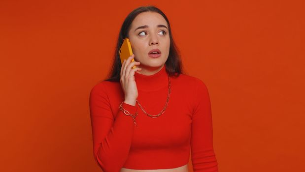 Lovely woman tired sleepy freelancer talking on mobile phone with friend, making online conversation. Disinterested sad young girl having annoyed boring talk on smartphone on red studio background