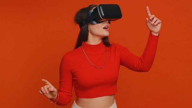 Lovely woman using headset helmet to play simulation game app online. Watching virtual reality 3D 360 video content. One girl in VR goggles isolated on studio red background. Futuristic technology
