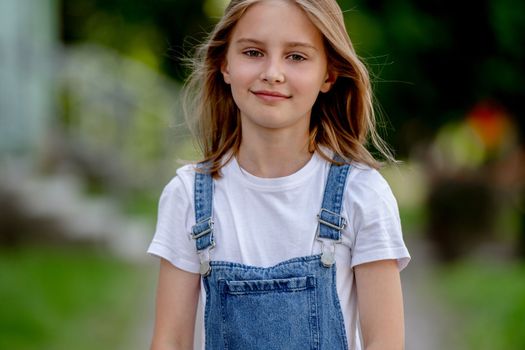 Beautiful preteen girl in city in summertime closeup portrait. Pretty female kid looking at camera in sunny day with blurred background