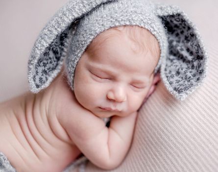 Cute newborn baby boy sleeping wearing bunny ears hat and knitted pants. Adorable infant child kid napping studio portrait
