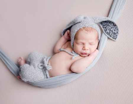 Cute newborn baby boy sleeping wearing bunny ears hat and knitted pants in hammock. Adorable infant child kid napping studio portrait