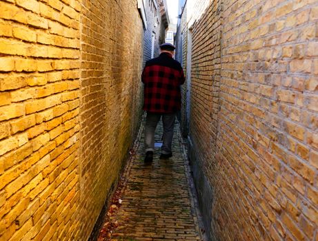 Man with broad shoulders walking down an an extreme narrow alley in Harlingen, the Netherlands