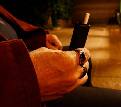 Fashionable man's hand with rings holding a black tobacco stick heater