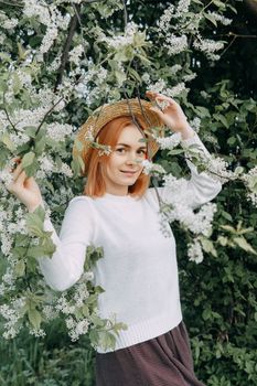 Portrait of a woman in a straw hat in a cherry blossom. Free outdoor recreation, spring blooming garden