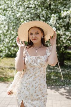 An attractive long-haired woman walks in the spring in the park of blooming apple trees. Spring portrait of a woman