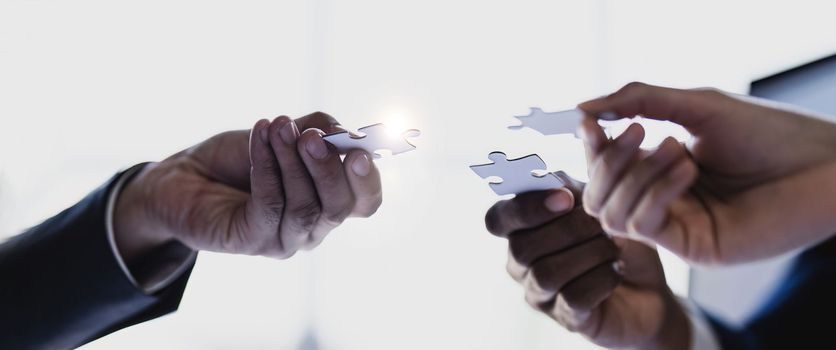 Business people with jigsaw puzzle pieces in office, Successful teamwork and partnership concept. hands holding pieces of white jigsaw puzzle.