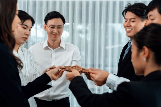 Closeup hand holding wooden gear by businesspeople wearing suit for harmony synergy in office workplace concept. Group of people hand making chain of gears into collective form for unity symbol.