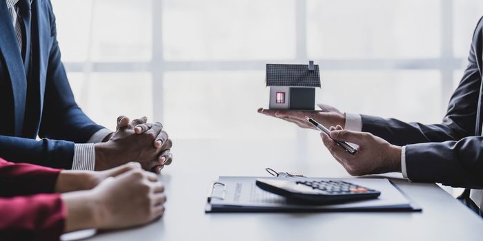 Real estate agent gives key to smiling clients. Happy couple signs papers and takes key to new home. Concept of young family making dream come true, buying house or getting apartment mortgage approval.