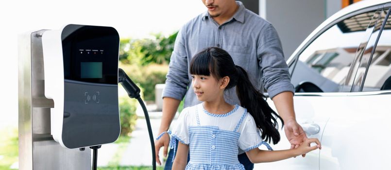 Progressive concept of a father and daughter who have just returned from school in an electric vehicle that is being charged at home. Electric vehicle driven by renewable clean energy.