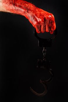 Faceless man holding handcuffs black background. Hands are stained with blood