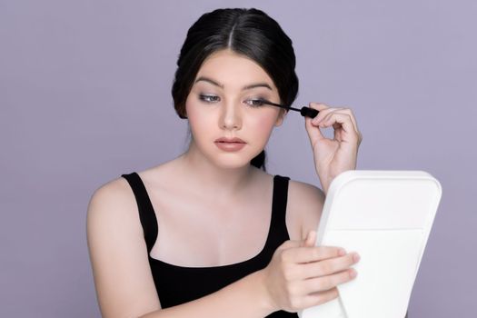 Beauty portrait of young girl applying eye mascara, eye makeup in front of mirror. charming young brunette girl posing gesture for eye cosmetic concept.