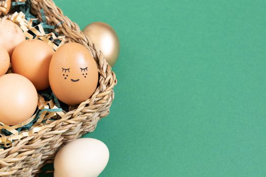 Easter eggs with funny face natural and gold in basket with paper filler . Branch of willow catkins. Light pastel orange background with copy space.