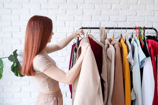 beautiful young woman in beige coat standing in front of hanger rack and choosing outfit dressing. Selection of a wardrobe, stylist, shopping. Clothes designing