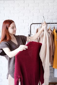 beautiful young woman in trendy outfit standing in front of hanger rack and choosing outfit dressing. Selection of a wardrobe, stylist, shopping. Clothes designing