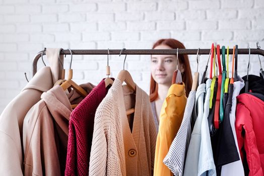 beautiful young woman in trendy outfit standing in front of hanger rack and choosing outfit dressing. Selection of a wardrobe, stylist, shopping. Clothes designing