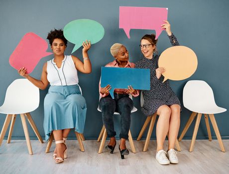 Are you sure about that girl. Studio shot of a group of attractive young businesswomen holding speech bubbles while sitting in a row against a grey background