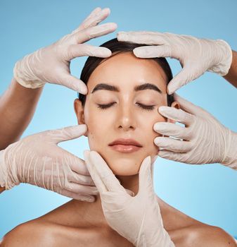 Plastic surgery, beauty and hands on the face of a woman isolated on a blue background in a studio. Feeling, skincare and doctors touching a model for a botox, cosmetics or dermatology consultation.