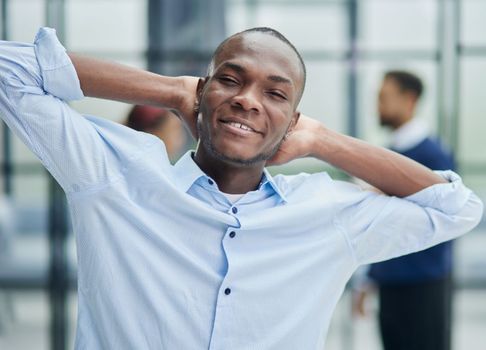 Happy african american young businessman holding hands behind head looking at camera