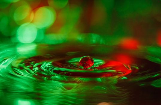 A transparent drop with a green background falls into the water. Abstract colorful background