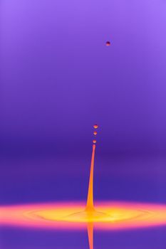 A drop falls into a thick liquid with a violet-yellow background. Abstract colorful background