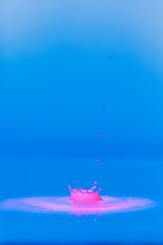 A drop falls into a thick liquid with a blue-pink background. Abstract colorful background