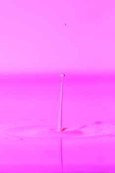 A drop falls into a thick liquid with a pink background. Abstract colorful background