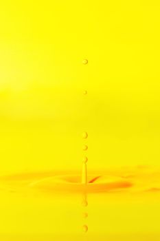 A drop falls into a thick liquid with a yellow background. Abstract colorful background