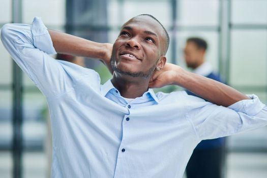 Happy african american young businessman holding hands behind head looking at camera