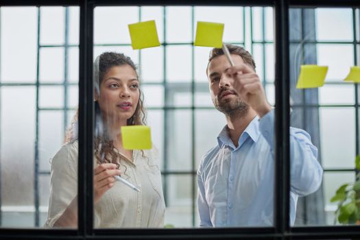 Creative professionals standing and discussing in office behind glass wall with sticky notes