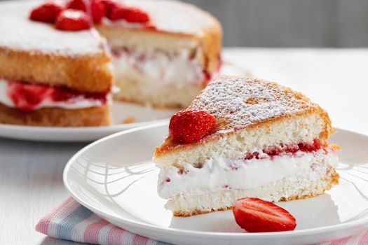 Piece of Victoria biscuit cake with whipped cream, jam and fresh strawberries.