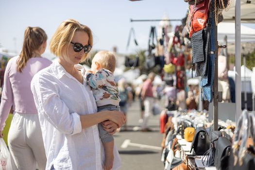 Mother hoding his infant baby boy child whilechecing items at sunday flea market