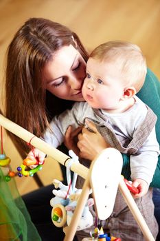 Hes so precious. Young mom giving her baby a cuddle while he plays