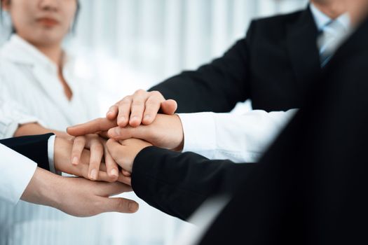 Closeup business team of suit-clad businessmen and women join hand stack together and form circle. Colleague collaborate and work together to promote harmony and teamwork concept in office workplace.