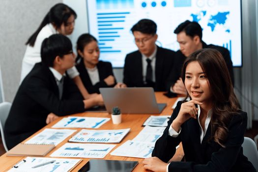 Focus portrait of female manger, businesswoman in the harmony meeting room with blurred of colleagues working together, analyzing financial paper report and dashboard data on screen in background.