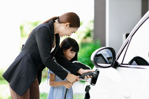 Progressive lifestyle of mother and daughter who have just returned from school in an electric vehicle that is being charged at home. Electric vehicle powered by sustainable clean energy.