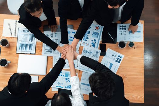 Top view cohesive group of business people join hands together, form circle over table filled with financial report paper. Colleagues working to promote harmony and team building concept in workplace.