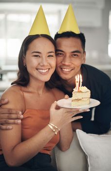 Portrait, birthday and cake with a couple in their home, holding dessert for celebration in party hats. Love, candle or romance with a young man and woman celebrating together in their house.