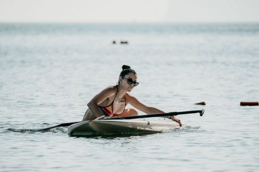 Sea woman sup. Silhouette of happy middle aged woman in rainbow bikini, surfing on SUP board, confident paddling through water surface. Idyllic sunset. Active lifestyle at sea or river