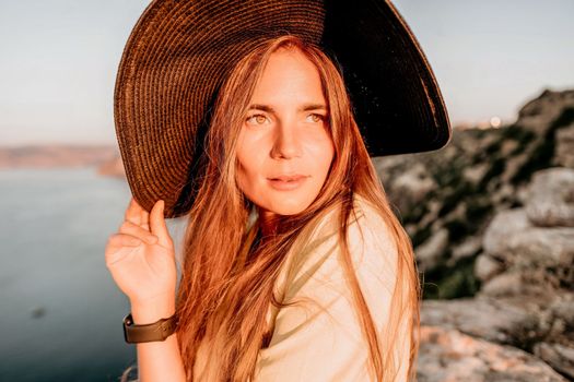 Portrait of happy young woman wearing summer black hat with large brim at beach on sunset. Closeup face of attractive girl with black straw hat. Happy young woman smiling and looking at camera at sea